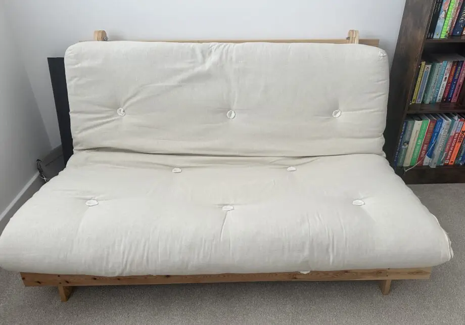 2 person Futon style sofa bed. Wooden frame and cream fabric cushion.