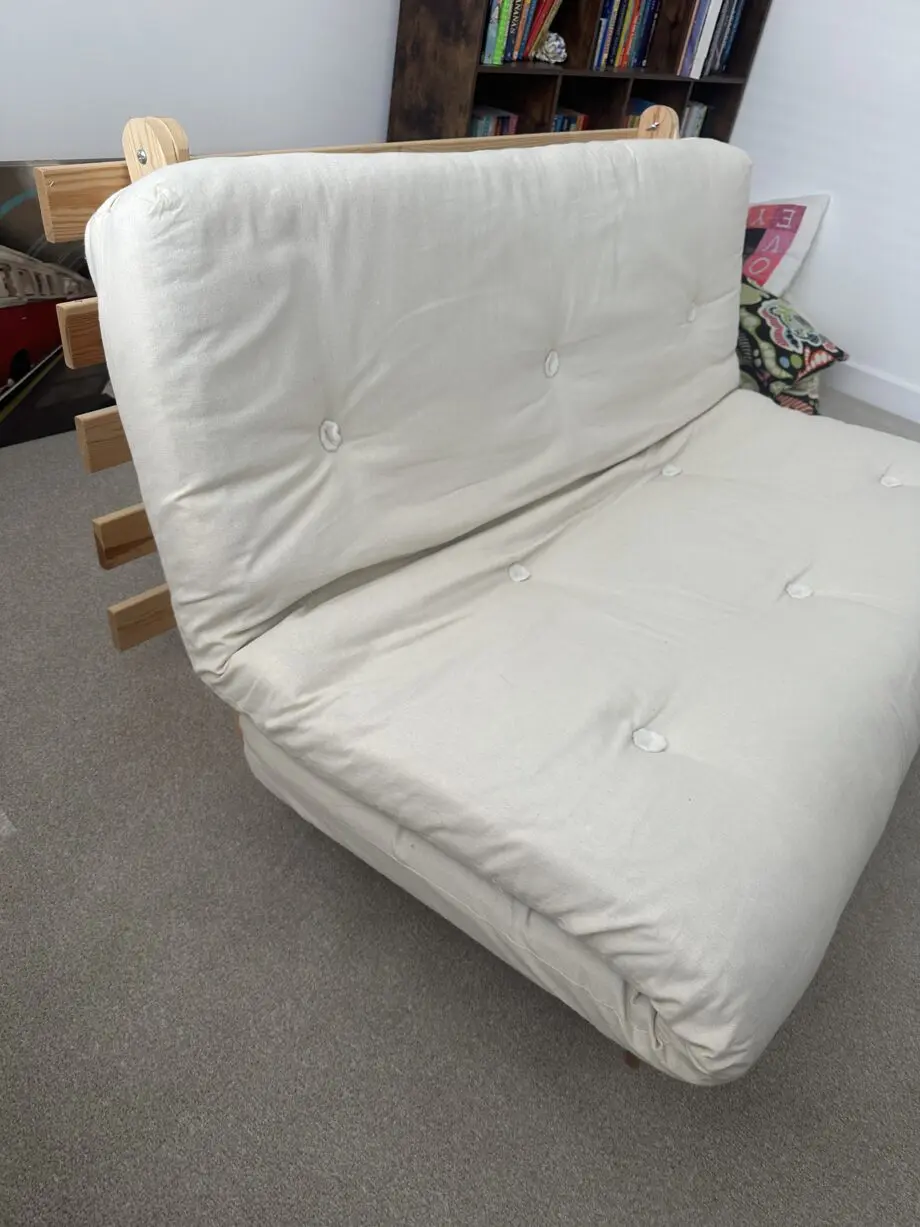 2 person Futon style sofa bed. Wooden frame and cream fabric cushion.