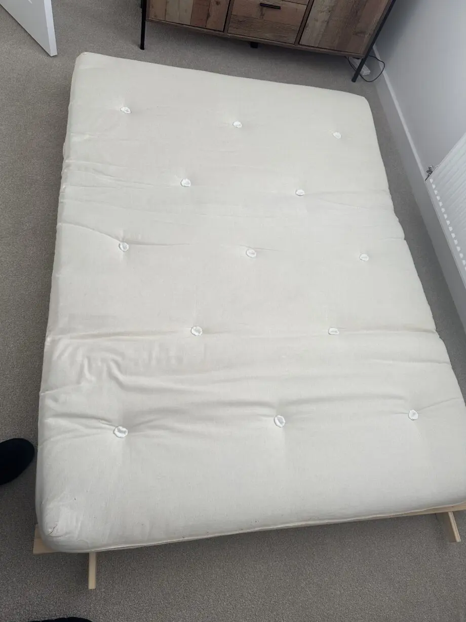 2 person Futon style sofa bed. Wooden frame and cream fabric cushion.
