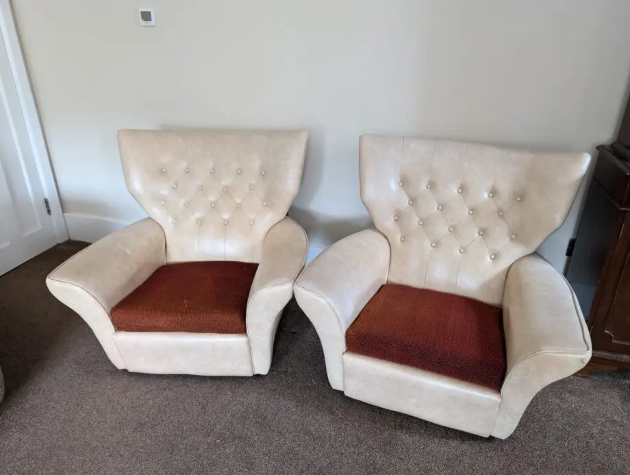 A pair of cream vinyl winged backed button arm chairs,