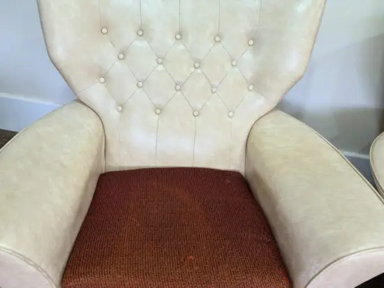 A pair of cream vinyl winged backed button arm chairs,