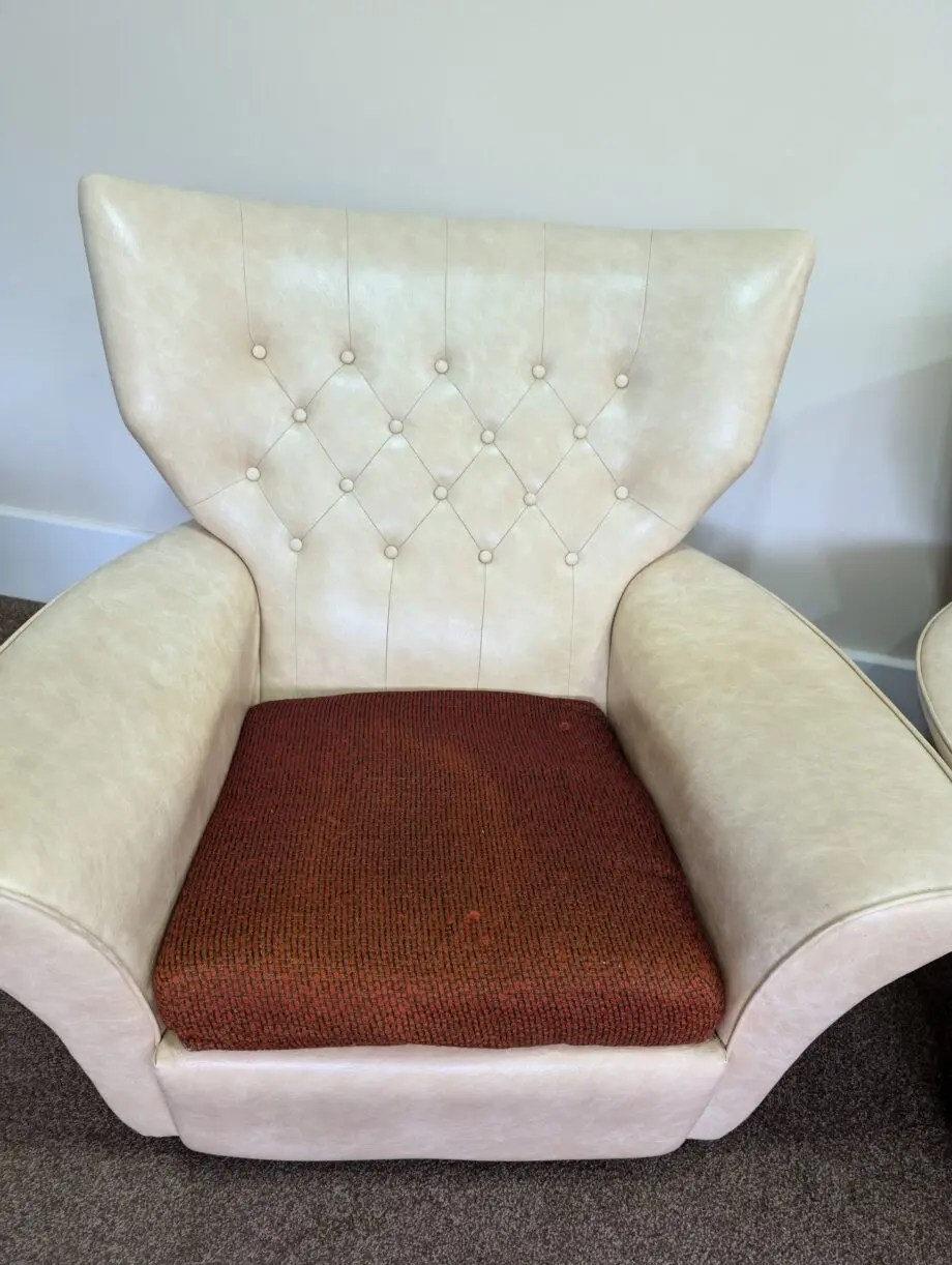 A pair of cream vinyl winged backed button arm chairs,
