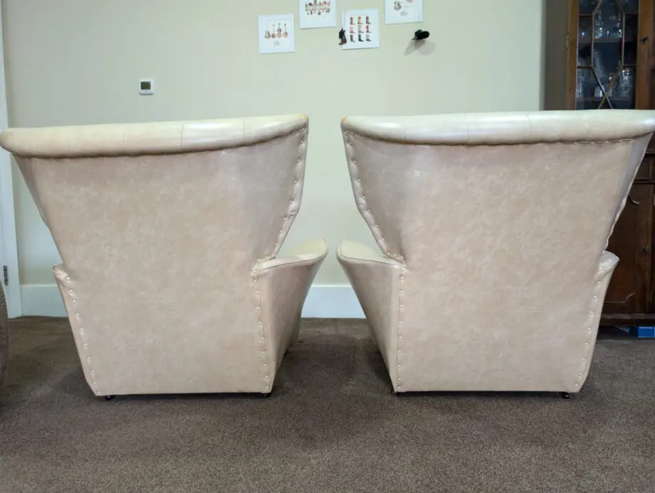 A pair of cream vinyl winged backed button arm chairs,