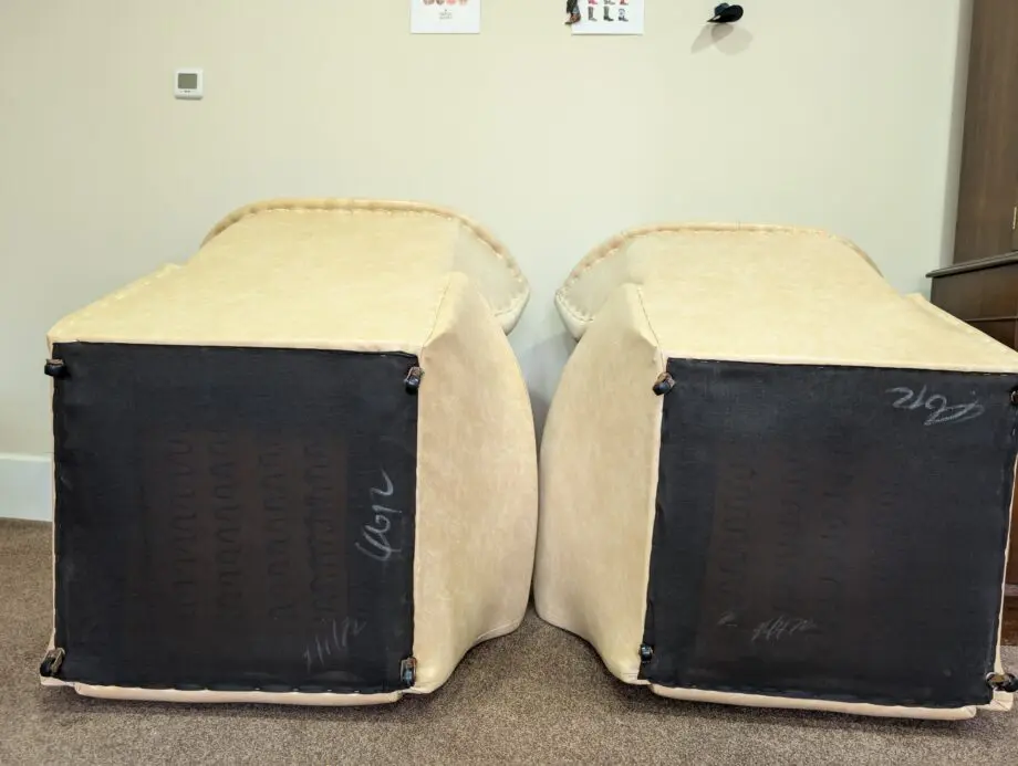 A pair of cream vinyl winged backed button arm chairs,