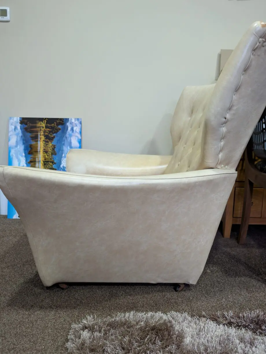 A pair of cream vinyl winged backed button arm chairs,