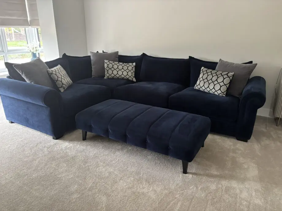 Large left hand corner sofa from Furniture Village. Navy blue with navy and grey scatter cushions included. Black feet. Matching footstool