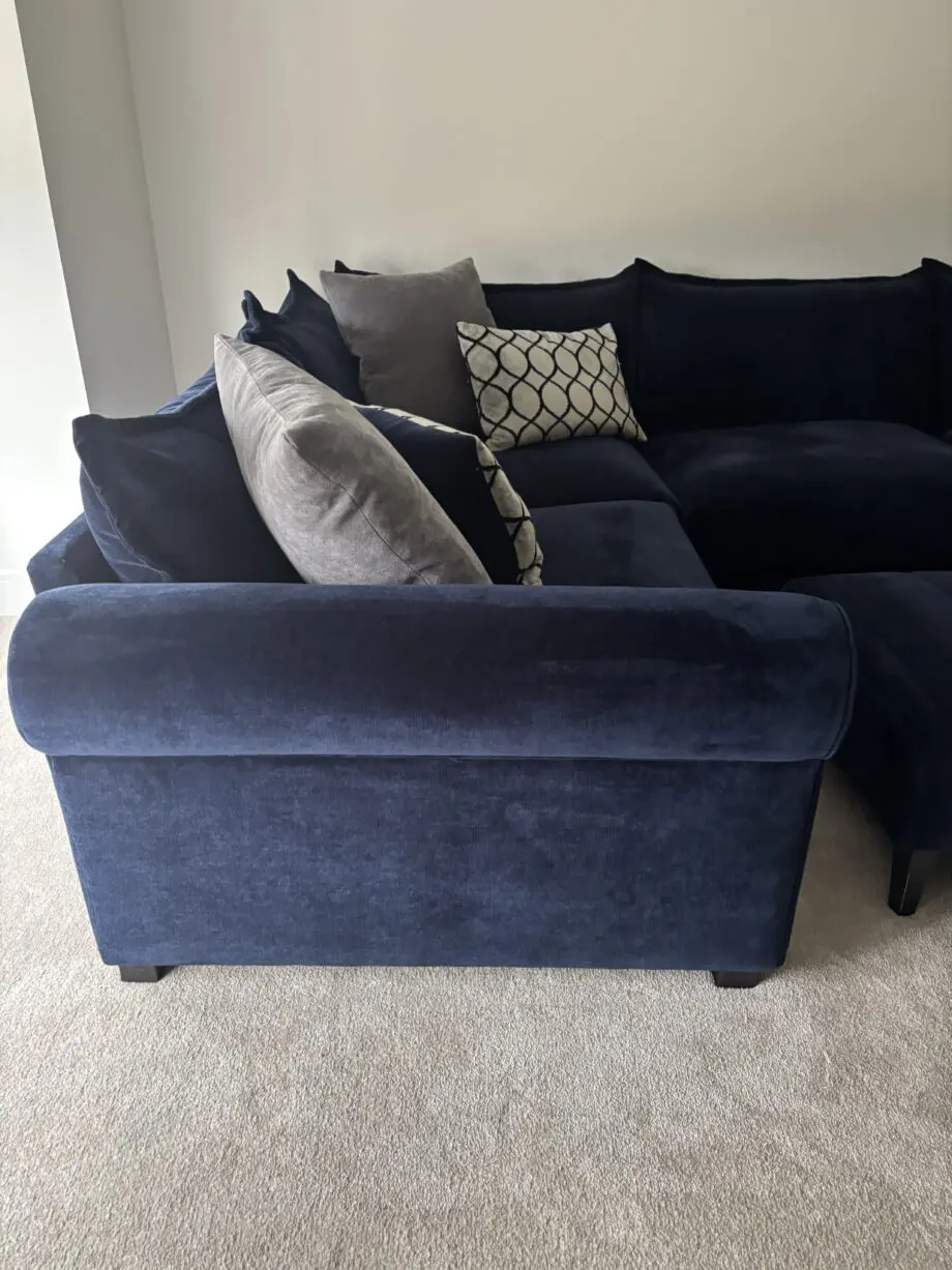 Large left hand corner sofa from Furniture Village. Navy blue with navy and grey scatter cushions included. Black feet. Matching footstool