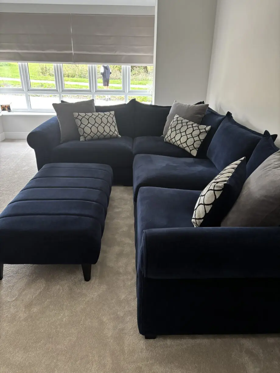 Large left hand corner sofa from Furniture Village. Navy blue with navy and grey scatter cushions included. Black feet. Matching footstool