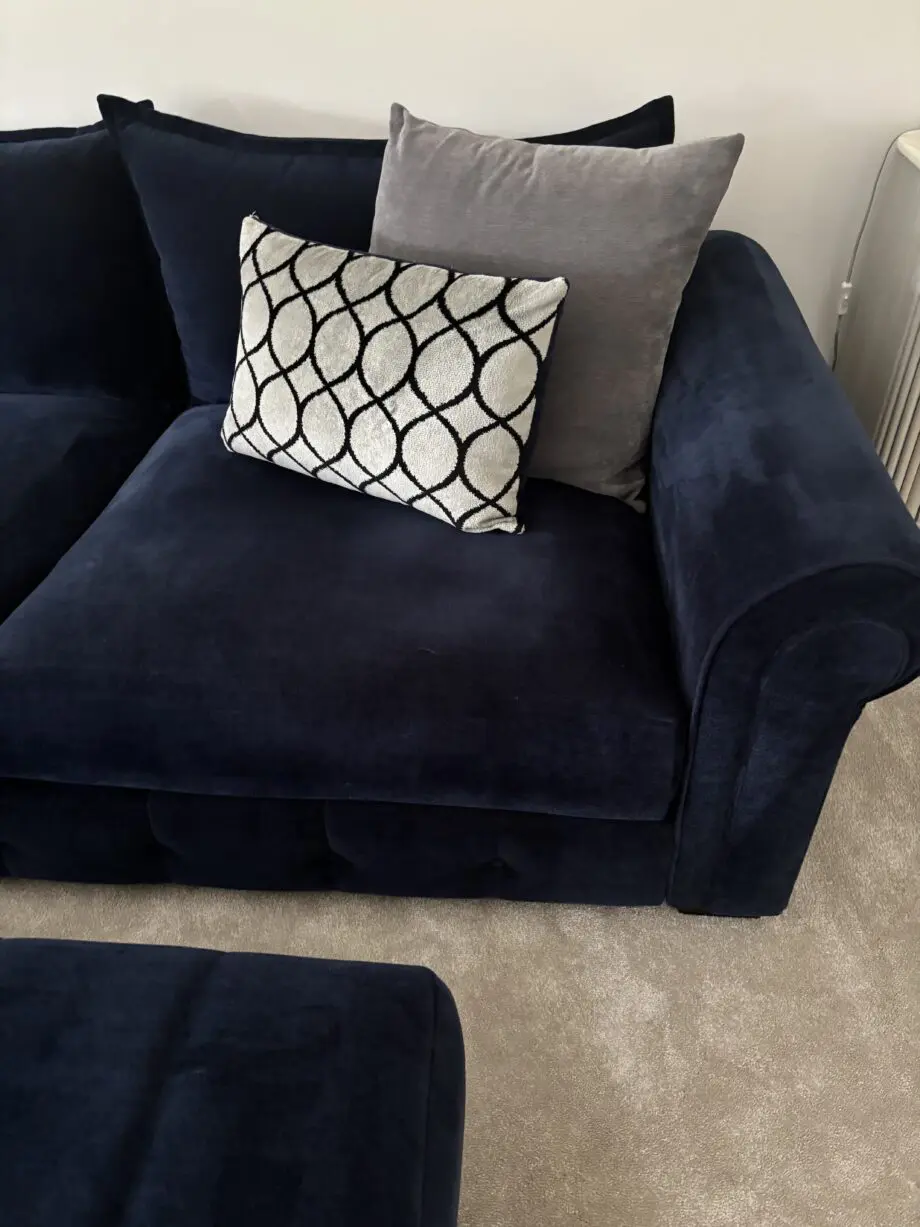 Large left hand corner sofa from Furniture Village. Navy blue with navy and grey scatter cushions included. Black feet. Matching footstool