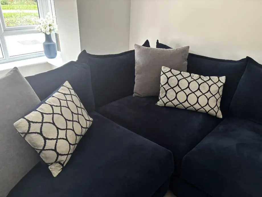 Large left hand corner sofa from Furniture Village. Navy blue with navy and grey scatter cushions included. Black feet. Matching footstool