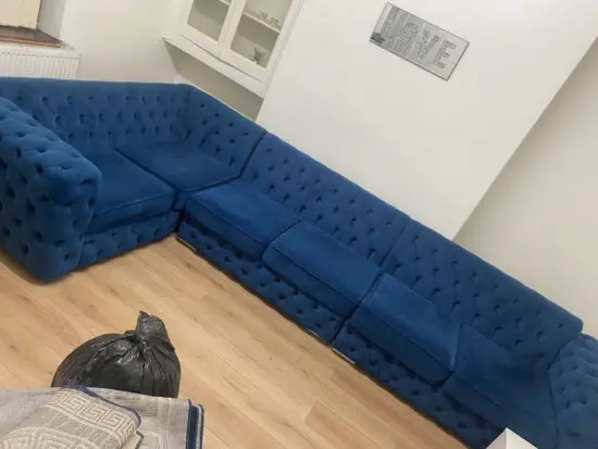 This is a blue plush velvet Chesterfield-style corner sofa.